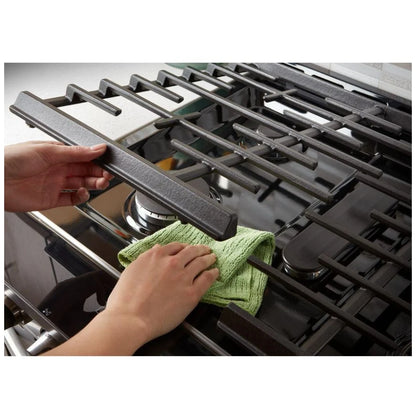 Close-up of a person cleaning the cast iron grates of the gas range, demonstrating ease of maintenance and care for long-lasting cookware.